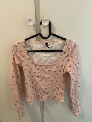 Ljusrosa blommig långärmad topp - Söt ljusrosa topp med små blommor och ribbad struktur. Toppen har lång ärm, rundad urringning och croppad passform. 