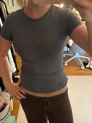 Mörkgrå tight t-shirt - Snygg mörkgrå t-shirt med tight passform och korta ärmar. Enkel och stilren design utan tryck eller mönster, perfekt till jeans eller mjukisbyxor. Materialet känns mjukt och stretchigt, troligen bomull eller en bomullsblandning. Skriv pm vid funderingar!☺️