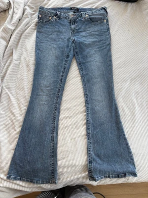 Blå bootcut jeans med utsvängda ben - Säljer ett par klassiska blå bootcut jeans med utsvängda ben och fem fickor. Jeansen har en snygg tvättad look och är tillverkade i denim. Perfekta för dig som gillar retrostil och vill ha ett par jeans som sticker ut.