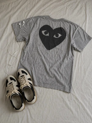 Grå Comme des Garçons PLAY t-shirt - Säljer en grå t-shirt från Comme des Garçons PLAY med svart tryck framtill och stort hjärta med ögon på ryggen. Äkta. Passar M.