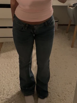 Blå bootcut jeans med broderade fickor - Säljer ett par blå bootcut jeans med snygga broderade detaljer på bakfickorna. Jeansen har låg midja och klassisk femficksdesign. Tillverkade i denim med lätt tvättad look och raka ben som går ut lite nedtill.