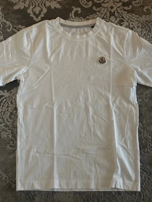 Moncler T-shirt  - Snygg fin vit Moncler t-shirt i bomull med rund hals och korta ärmar testad bara nyskick. Perfekt till jeans eller shorts för en avslappnad stil, pris kan diskuteras vid snabb affär.