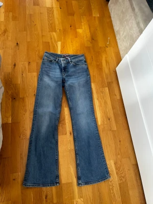 Blå bootcut jeans med hög midja - Säljer ett par klassiska blå bootcut jeans med hög midja och fem fickor. Jeansen har en snygg tvätt och vida ben som ger en retrovibe. Perfekta att styla med sneakers eller boots för en chill look.