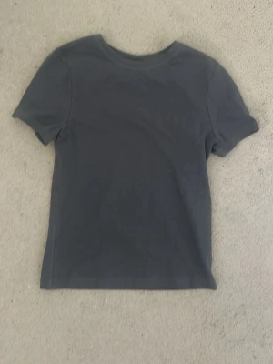 Mörkgrå basic t-shirt - En enkel och stilren mörkgrå t-shirt med rund hals och korta ärmar. Perfekt till jeans eller shorts för en clean look. Tillverkad i mjuk bomull som känns skön mot huden.
