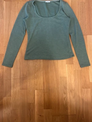 Grön ribbad långärmad topp - Snygg grön ribbad topp med lång ärm och rundad, djup urringning. Perfekt att styla med jeans eller kjol för en enkel men trendig look.