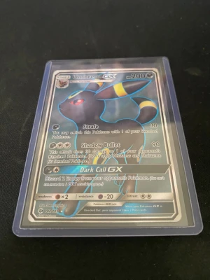 Pokémonkort Umbreon GX & Slowbro - Två Pokémonkort i plastfickor: Umbreon GX med mörkblå och gula detaljer samt Slowbro med rosa och blå färger. Båda korten har holografiska effekter och tydliga illustrationer av respektive Pokémon. Perfekt för samlare eller Pokémonfans.