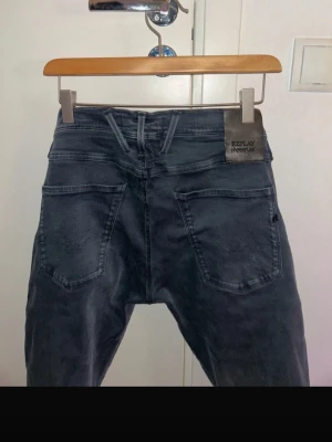 Replay jeans - Säljer ett par svarta Replay Hyperflex jeans med klassisk femficksdesign och snygga detaljer på fickorna. Jeansen har en slim fit passform och är tillverkade i stretchigt material för extra komfort. Perfekta för dig som vill ha både stil och rörlighet. 29/32