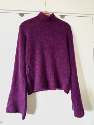 Plommonlila stickad tröja Gestuz, 72% mohair ull - storlek XS / S - Underbar lila stickad tröja från Gestuz i storlek XS (passar även S). Tidlös modell med långa trumpetärmar och polokrage. Fluffigt mjukt garn i 72% mohair ull, så bra naturmaterial som andas. Lika snygg som den är eller med ett skärp i midjan. Nypris 2799:-. Mycket gott skick, som ny!