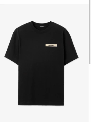 Svart Jacquemus t-shirt i bomull, oanvänd i Storlek L - Säljer en svart t-shirt från Jacquemus med diskret logga på bröstet. Klassisk passform och rund halsringning. Tillverkad i mjuk bomull som känns skön mot huden. Perfekt för dig som gillar stilrena och trendiga plagg.  Oanvänd i storlek L