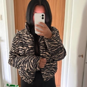Zebramönstrad pufferjacka H&M S - Säljer en zebramönstrad pufferjacka från H&M i storlek S. Jackan har svart och beige mönster, hög krage och dragkedja framtill. Perfekt för dig som vill sticka ut med en trendig och varm vinterjacka. Materialet är syntet och jackan är vadderad.