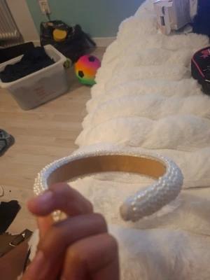 Vitt diadem med pärlor - Säljer ett snyggt vitt diadem täckt med små pärlor. Diademet har en vadderad form som ger volym och en lyxig känsla. Perfekt accessoar för att lyfta din look med en elegant touch.