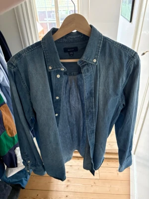 Blå jeansskjorta från Gant - Riktigt fet denim skjorta från Gant. Mycket bra skick använd max 3 ggr. Storlek 16 år vilket motsvarar en S. 