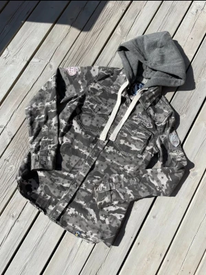 Superdry camo jacka - Jacka med hoodie camo mönster. Gott skick inga hål eller fläckar.