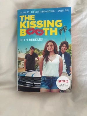 The Kissing Booth av Beth Reekles - En ungdomsroman med färgstarkt omslag där tre tonåringar står framför en bil och palmer. Boken är på engelska och handlar om Elle Evans och hennes liv som vänds upp och ner efter en kyss med skolans bad boy. Omslaget har blå bakgrund och gula bokstäver.