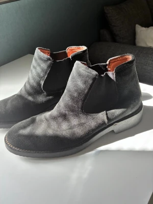 Chelsea boots mocha svart - Ett par klassiska Chelsea Boots i svart mocka. Skorna har resårpaneler på sidorna för enkel på- och avtagning samt en bekväm passform. Yttersulan har ett vågigt mönster för bra grepp. Dessa boots är ett mångsidigt tillskott till garderoben.