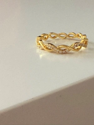 Guldfärgad flätad ring i rostfritt stål med stenar - Snygg guldfärgad ring i rostfritt stål med flätad design och glittriga små stenar längs ena sidan. Ringen har en elegant och modern look med twistad form som ger extra detalj. Perfekt för dig som gillar stilrena accessoarer med lite bling.storlek 16,5mm