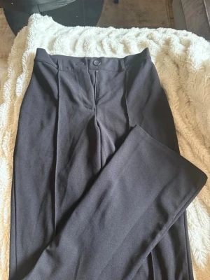 Svarta kostymbyxor från Bubbleroom - Stilrena svarta kostymbyxor från Bubbleroom med raka ben/bootcut och pressveck. Byxorna har hög midja, dragkedja och knapp framtill. 