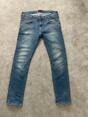 Blå slim fit jeans med slitningar - Snygga blå slim fit jeans från Lee med lätt slitna detaljer på framsidan och klassiska fem fickor. Jeansen har en något tvättad look och raka ben. Perfekta för en avslappnad och trendig stil. Priset kan diskuteras!