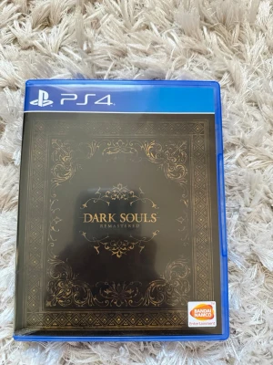 Dark Souls Remastered PS4 spel - Säljer Dark Souls Remastered till PS4. Spelet kommer i ett blått plastfodral med snyggt svart och guldigt omslag. Skivan har tryck med spelets logga och mörka motiv. Perfekt för dig som gillar utmanande action-RPG och episka äventyr. Alla dlc inkluderat