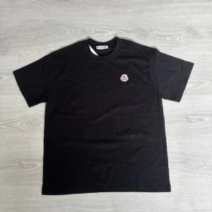 Svart Moncler t-shirt med logga - Snygg svart t-shirt från Moncler med klassisk rund hals och liten Moncler-logga på bröstet. T-shirten har korta ärmar och är gjord i mjuk bomull för en skön känsla. Perfekt till jeans eller shorts för en clean look.