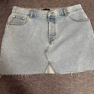 Kort jeans kjol  - Helt ny oanvänd kort jeanskjol från ASOS med slitna detaljer i storlek EU44. 