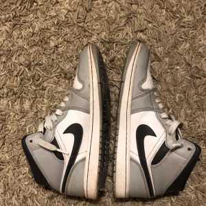 Jordan 1 Mid Light Smoke Grey Anthracite  - Ett par sparsamt använda Jordan 1 sneakers. Dom blev inköpta i år i mars någon gång. Dom har en skada på undersidan av skon som är liten. Man märker inte av den något alls! Jag har lådan till! 