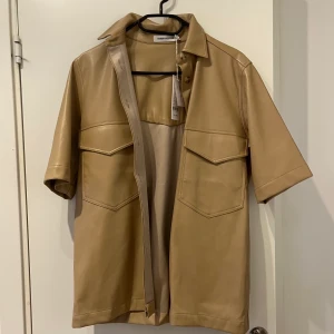 Skjorta i läderimitation  - Beige skjorta i fakeskinn från Carin Wester i nyskick, endast provad.