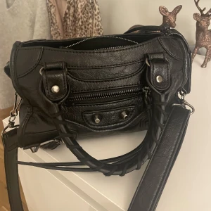 Svart handväska  - Säljer denna super fina väskan som jag köpt på Plick för bara någon månad sedan. Väskan är varsamt använd och ser så gott som ny ut. Fack finns och spegel kommer med. Skriv vid intresse, vill få sålt den snabbt❤️