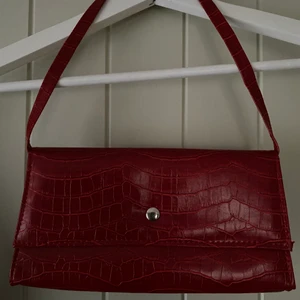 Röd vintage väska i ormskinnsimitation  - Säljer min snygga röda väska som passar till verkligen alla situationer! Tyvärr kommer den inte längre till användning hos mig, den är köpt second hand och därav vet jag inte märke. Väskan är i mycket gott skick och har 3 fack inuti. Längd: 25 cm Djup: 3 cm Höjd: 12 cm. Det är bara att höra av sig vid frågor och funderingar! Kan fraktas och priset går att diskutera💚