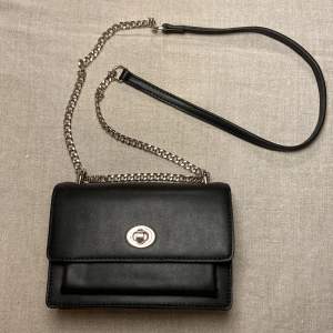 En svart handväska med silvrig kedja, helt oanvänd och i nyskick, den har två stora fack med ett mindre fack i ena, super söt fast säljer pga kommer inte till användning 