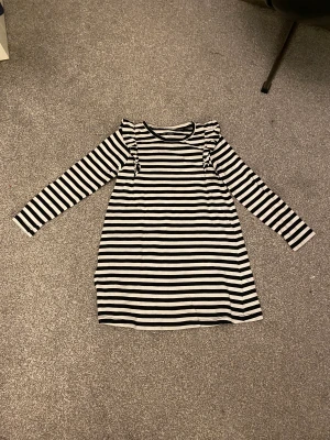 Randig klänning med volang - Säljer denna svart, vit randiga klänningen med volang som är i storlek 122 använd ganska mycket när jag var liten men den är som ny inga fläckar, hål eller andra skador. Den kostar 40kr + frakt såklart❤️ från Lindex 