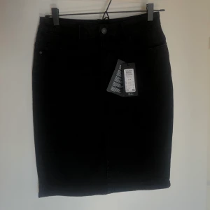 Svart jeanskjol Vero Moda - Svart längre jeanskjol från Vero Moda, tajtare men väldigt stretchig. 5-ficksmodell, liten slit baktill. Storlek M. Aldrig använd (prislapp kvar) inköpspris 200 sek.  