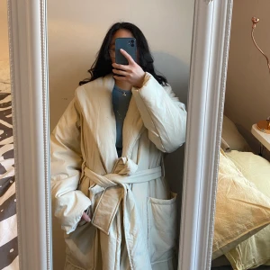 Lång piffig jacka - Jackan är köpt från Gina Trico på rea för lite under 260kr en varm jacka med skärp använt endast en gång. Säljer då jag redan har många vita puffiga jackor och detta var ett impulsivt köp. Jag är 157, den är en decimeter från marken när jag har på mig den