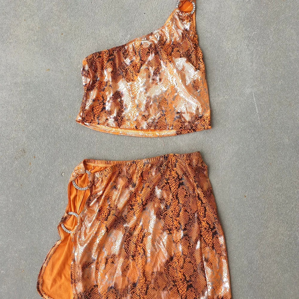 Did someone say Euphoria? Beautiful micro mini skirt and top set in orange and silver snake print. Pre-loved condition. Silver sparkle charms. . Kjolar.