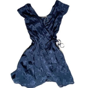 Söt klänning - Suuperfin blå knyt-klänning i lite satin-liknande tyg💗 blommig mönster som skimrar, köpt på sellpy men aldrig använd! ungefär 72 cm lång 