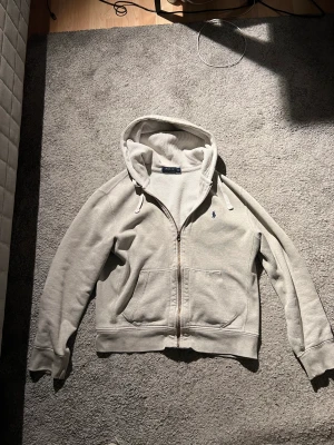 Grå Ralph lauren zip Hoodie - En grå Ralph lauren zip Hoodie i storlek M. Den är i bra skick syns knappt att den är använd. Nypris ligger på runt 1300kr. Jag säljer den för 600kr 