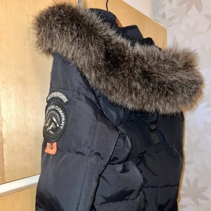 SuperDry dunjacka strl 36 - Sparsamt använt, i mycket bra skick. Strl 36, perfekt fodrad vinterjacka! Svart, med fuskpäls. Kan både mötas upp i Stockholm eller frakta från Stockholm. Nypris ca 1000kr. Pris kan eventuellt diskuteras.