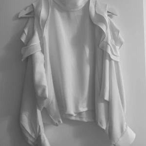 Blus med öppna axlar  - Blus med hög krage, öppna axlar och volanger. Storlek M-L  80 kr