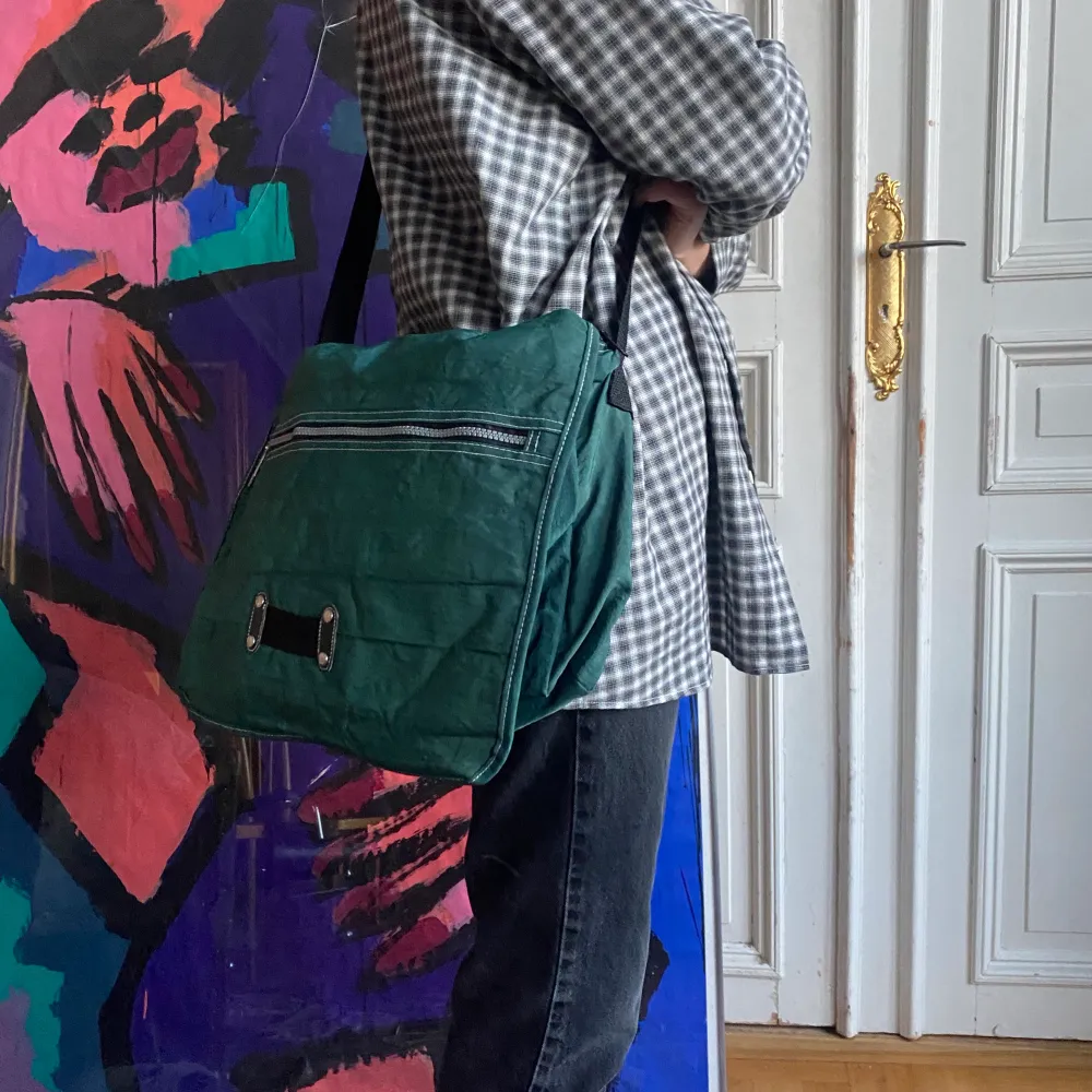 En grön axelremsväska med många fack och blixtlås i tyg. Väskor.