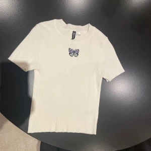 En t-shirt från hm i storlek XS - Jag säljer min vita t-Shirt från hm med en fjäril på i storlek xs. Den är i ett Stretchigt material som jag har använt väldigt sällan. Köparen står för frakten om vi inte möts upp i Kungälv.