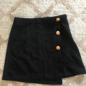 Svart omlottkjol  - En fin svart omlott kjol med guldfärgade knappar som detaljer. Storlek xs. Från SHEIN. Jag skickar den som ett brev via PostNord. 