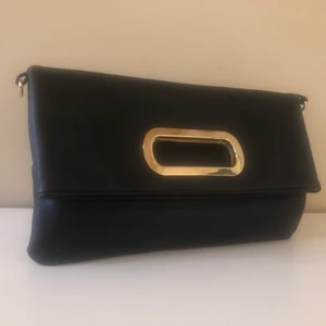 Svart handväska med gulddetalj - Svart handväska med ett guldhandtag. Finns två fack, ett större och ett mindre🌸 Finns även två små fack och ett fack med dragkedja i det stora facket! Köpt i London och är knappt använd 😊