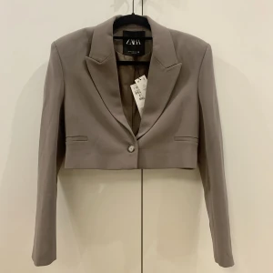 Kort kavaj, Zara. Strl. XS - Brun kavaj i kortare modell från Zara. Storlek XS. Helt oanvänd med prislappen kvar. Nypris 599kr