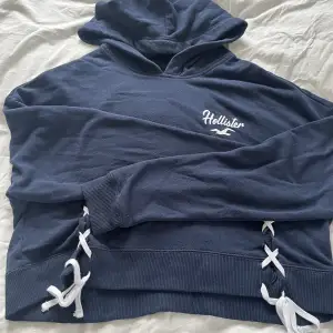 En marinblå hoodie från hollister med coola detaljer. Fint tryck på ryggen. Den är xs, men passar fint på mig som brukar ha m med bara att den är lite mer croppad då.🥰