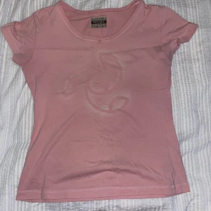 Rosa t-shirt  - Säljer min fina t-shirt som tyvärr inte passar länge. Den har vita sömmar och ett mönster framtill. Det finns en liten fläck vid kragen på framsidan (syns på bild 1) men skulle inte säga att det är något man tänker på, annars är den i fint skick!