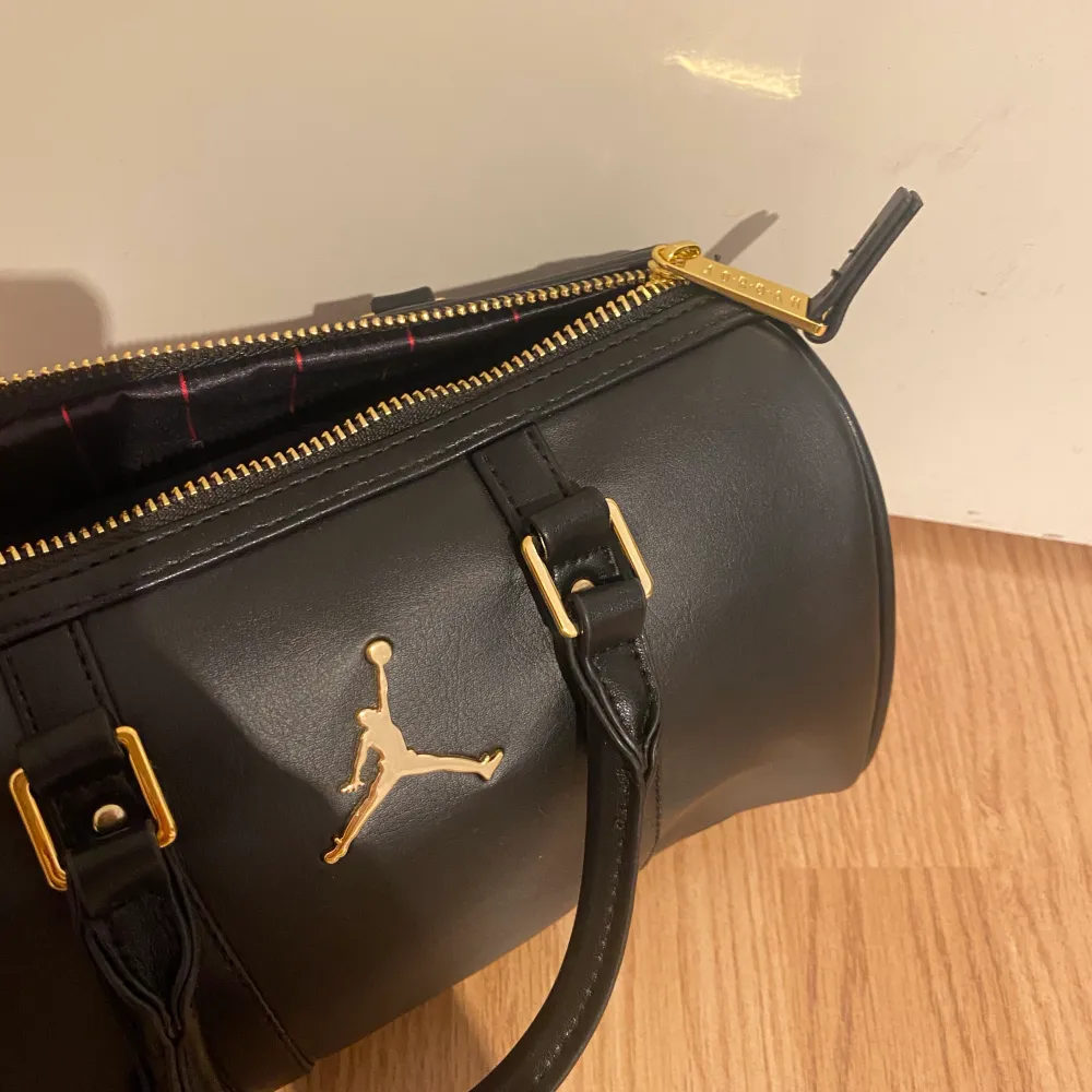 Äkta Nike Jordan handväska/axelväska, aldrig använd. Svart med guldfärgade detaljer. 10x22 cm. Jättesöt. Aldrig använd, lappen sitter kvar.. Väskor.