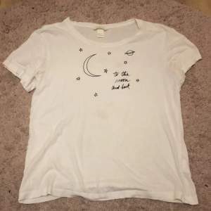 En t-shirt från hm med tryck där det står ”to the moon and back” tillsammans med en måne, en planet och små stjärnor. Det finns en liten fläck på framsidan som knappt syns.
