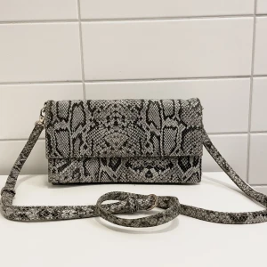 Väska med axelband - Väska i skinn från Gestuz i grått ormmönster. Den har tre fack, två lite större och ett litet mindre med dragkedja (obs väskan är dock inte särskilt stor). Syns inte toppen på bilderna men spännen är ljust guldiga. ⭐️