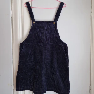 Manchesterklännig Monki  - Tjusig manchesterklänning i mörkblå/petrolblå kulör. Bred manchester. Reglerbara hängslen i 2 olika lägen. Fickor. Når ungeför ner till mitten på låret. Nyskick! Anvönd en enda gång. 
