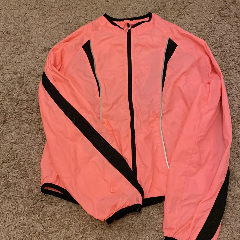 Det är en rosa jacka med svara detaljer och man brukar oftast ha den när man tränar . Jackor.